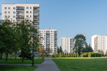 A large public park with a green lawn and trees located in a high-density housing estate. A walking path winds through this recreational space, with tall blocks of flats in the background.