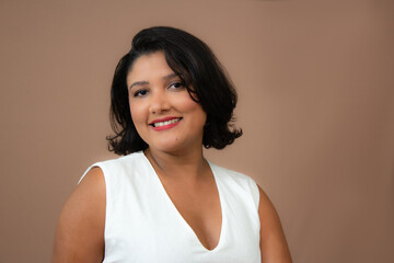Charming businesswoman in white top smiling at camera. Perfect for professional development,  soft skills, career, personal growth. Horizontal studio portrait with copy space on brown background.