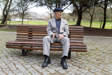 Elderly gentleman sitting on bench in park contemplating nature