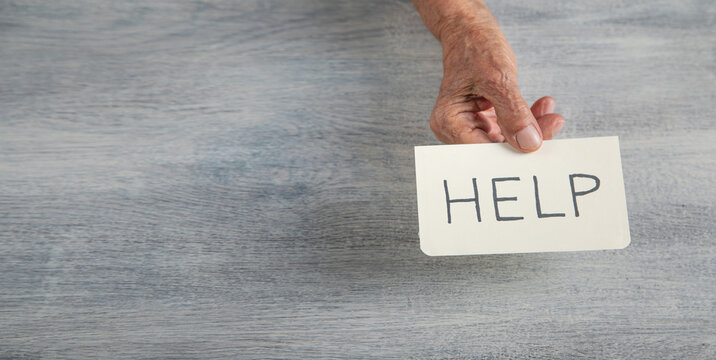 Elderly female hand with a Help message on paper.