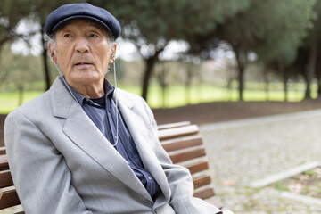 Fototapeta premium Elderly asian man listening music with earphones sitting on bench in park