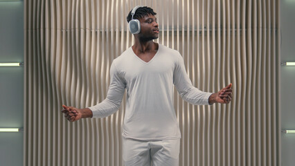 Young African American guy male man wearing headphones dancing to music in white modern futuristic...