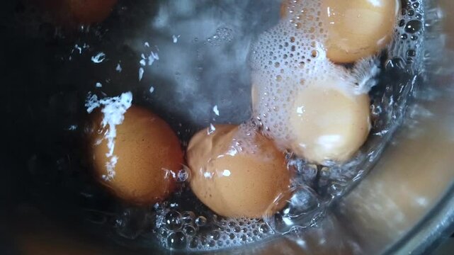 Six eggs boil in a saucepan filled with bubbling water on a stovetop. A close-up kitchen scene ideal for recipe videos, cooking tutorials, food content, or domestic lifestyle footage.