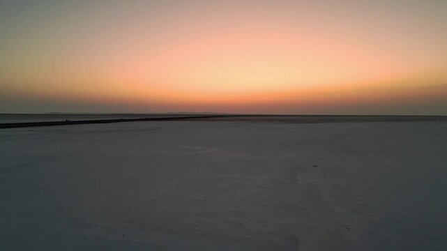 An aerial view of the Rann of Kutch, Gujarat, India reveals an endless white salt desert glowing under a vibrant sunset, casting warm hues across the vast 4K