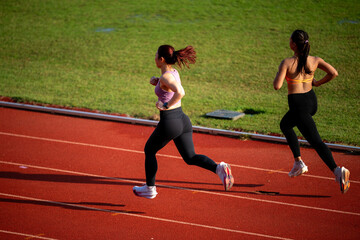 Two women running on a track. One is wearing a purple shirt. The other is wearing a yellow top