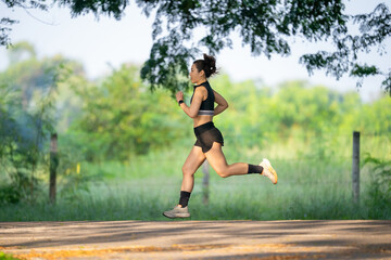 A woman is running on a road. She is wearing a black shirt and shorts. The road is surrounded by trees