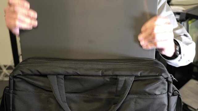Businessman is putting his laptop into his briefcase and closes the zipper. 