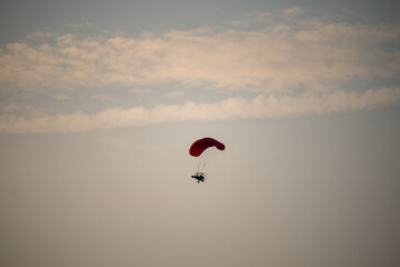 A red parachute is flying in the sky. The sky is cloudy