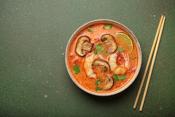 Delicious tom yum soup with shrimps, mushrooms, lime, and coriander served in bowl with chopsticks...