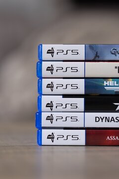 Brecht, Belgium - 18 april 2025: A vertical portrait of a stack of multiple sony playstation 5 videogame cases or boxes lying on a wooden table. Ready to play a console game.