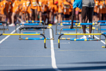 Several hurdles placed on a blue running track with a group of athletes in orange shirts waiting behind
