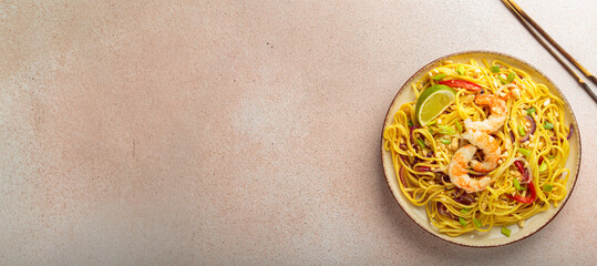 Delicious pad thai dish with shrimps, peanuts, lime and chopped vegetables, chopsticks on light...