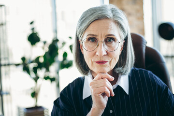 Confident mature businesswoman in formal attire seated in modern office, showcasing professionalism...