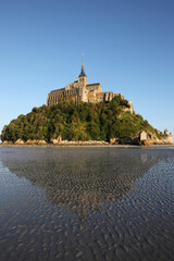 view of famous Le Mont Saint-Michel tidal island with clear water and beautiful reflections on a sunny day, Normandy, northern France