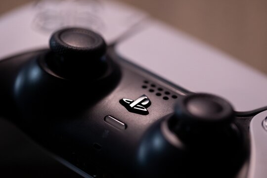 Brecht, Belgium - 18 april 2025: A portrait of a white original sony playstation 5 wireless controller lying on a wooden table with the focus on the PS logo. Ready to play a console video game.