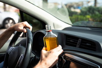 Man holding a bottle of alcohol while driving a car, highlighting the danger and irresponsibility...