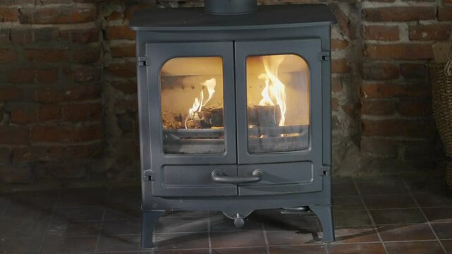 A black stove with a brick wall behind it. The stove is lit and has a fire in it