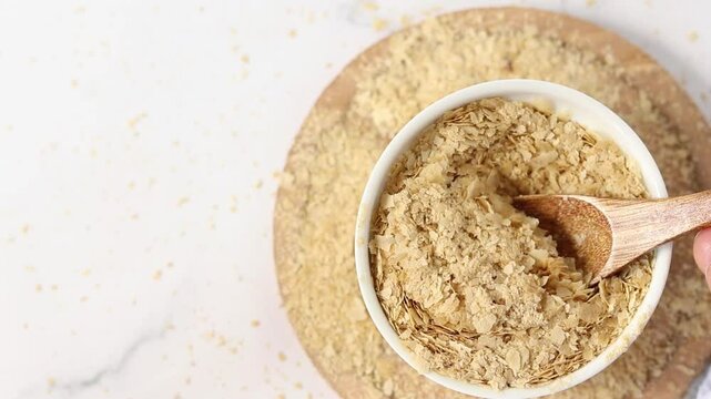 Nutritional yeast flakes in a bowl with wooden spoon. Top view. Vegan cheese substitute.