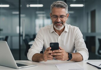 Middle aged Hispanic business manager ceo using cell phone mobile app, laptop. Smiling Latin or Indian mature man businessman holding smartphone sit in office working online on gadget with copy space.