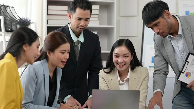 A group of people are gathered around a laptop, working together on a project. The atmosphere is collaborative and focused, with everyone contributing their ideas and expertise