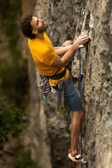A man in a yellow shirt is climbing a rock wall