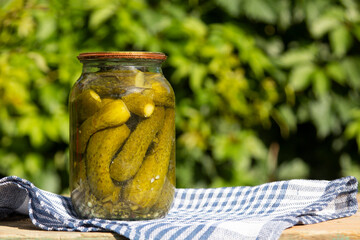 Jar of homemade preserves cucumbers on wooden table against nature background.  Copy space. 