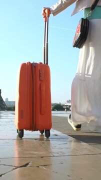 Woman rolling orange suitcase in sunlight. Excitement of travel, the freedom of departure, and the anticipation of a new destination. Escape, change, and the beginning of a new story.
