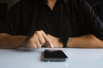 Man pointing at smartphone screen on table, digital interaction and modern technology concept, close-up in dark tone.