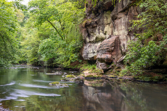 Roslin Glen, East Lothian, Scotland in Spring &mdash; Tranquil River North Esk Winding Below Sheer Stone Cliffs, Surrounded by Dense Fresh Foliage and Mossy Banks in Serene Natural Canyon Setting
