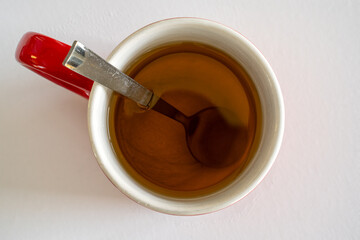 Mug with tea and a spoon inside, as viewed from top on a white background.