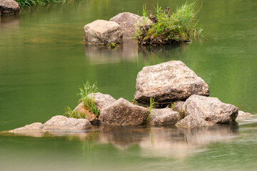 Litttle stone islands in a river with green water on a rainy day.
