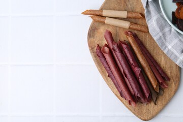 Tasty fruit leather rolls on white tiled table, flat lay. Space for text