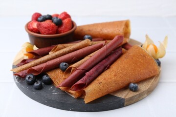 Delicious fruit leather rolls and berries on white table, closeup