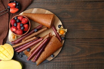 Delicious fruit leather rolls, mango and berries on wooden table, flat lay. Space for text
