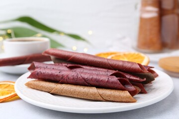 Tasty fruit leather rolls on white table, closeup