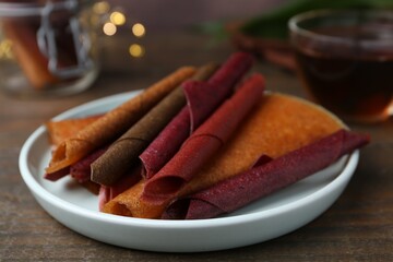 Tasty fruit leather rolls on wooden table, closeup