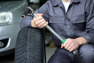 Mechanic with wrench and tire at car service, closeup