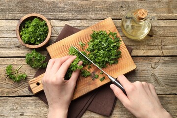 Woman cutting parsley at wooden table, top view