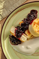 Cheesecakes with berry sauce and sour cream lying on green plate