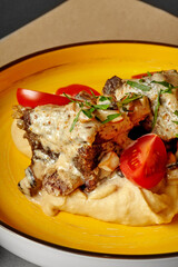 Beef bourguignon with creamy mushroom sauce, mashed potatoes and cherry tomatoes on yellow plate