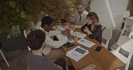 A diverse business team collaborates on a project in a modern cafe, analyzing charts and discussing strategies. - Powered by Adobe