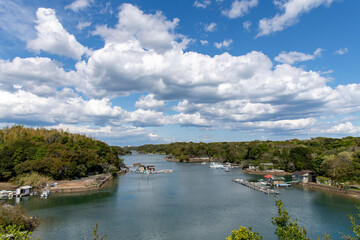 High level panoramic view over one of the bays of the Shima peninsula, Mie, Japan with small floating fishing settlements and large white cumulus clouds in blue sky