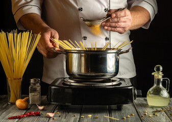A chef adds seasoning to a pot of boiling water filled with pasta. Dried spaghetti and ingredients...