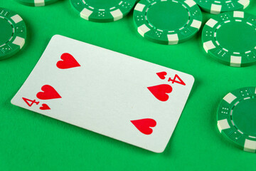 A single red card with a heart and the number four lies on a bright green surface surrounded by green poker chips, suggesting an active poker game