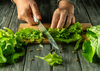 Hands skillfully chop crisp lettuce on a wooden cutting board, surrounded by vibrant green leaves,...