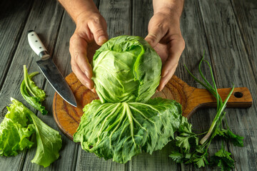 Hands are holding a vibrant head of lettuce above a wooden cutting board. Nearby, chopped cilantro...