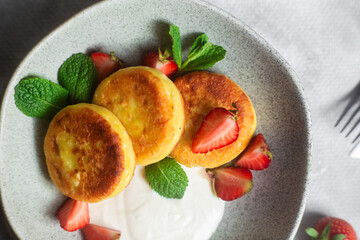 Syrniki Cheesecakes Appetizing cottage cheese pancakes with cream sauce, strawberries and mint in a...