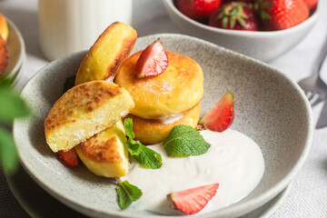 Syrniki Cheesecakes Appetizing cottage cheese pancakes with cream sauce, strawberries and mint in a...