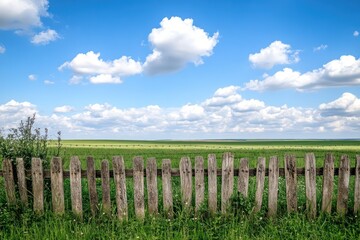 Fototapeta premium Rustic wooden fence with barbed wire and open field under blue sky