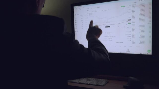 A man is sitting in front of a computer monitor. He is looking at the screen. The screen is black and white